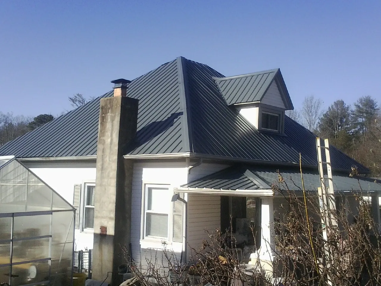 Dark blue standing seam metal roof on a white farmhouse with dormer — Slate & Tile Roof Repair by Roofing Brothers in Kirklin
