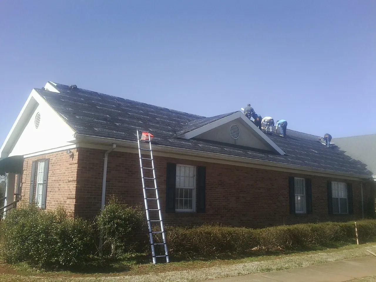 Crew tearing shingles off a brick ranch roof with a ladder set — Emergency Roof Repair work by our crew in Kirklin
