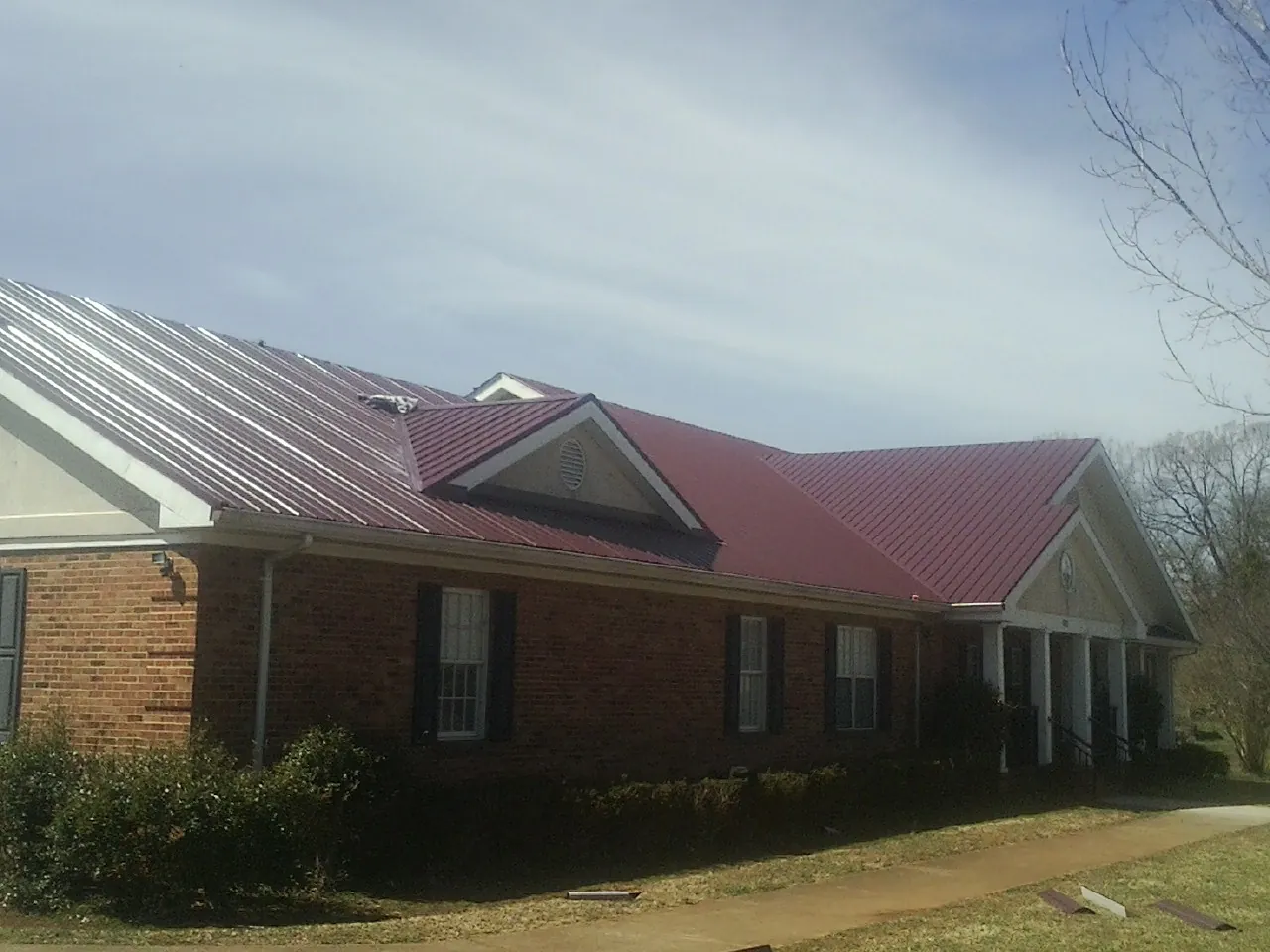 Red metal roof with gabled entries on a long brick building, from a Hail Damage Roof Repair job in Kirklin