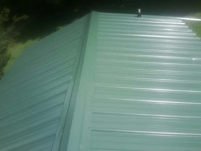 New green metal panels meeting at the ridge of a roof — Flat Roof Repair work by our crew in Kirklin