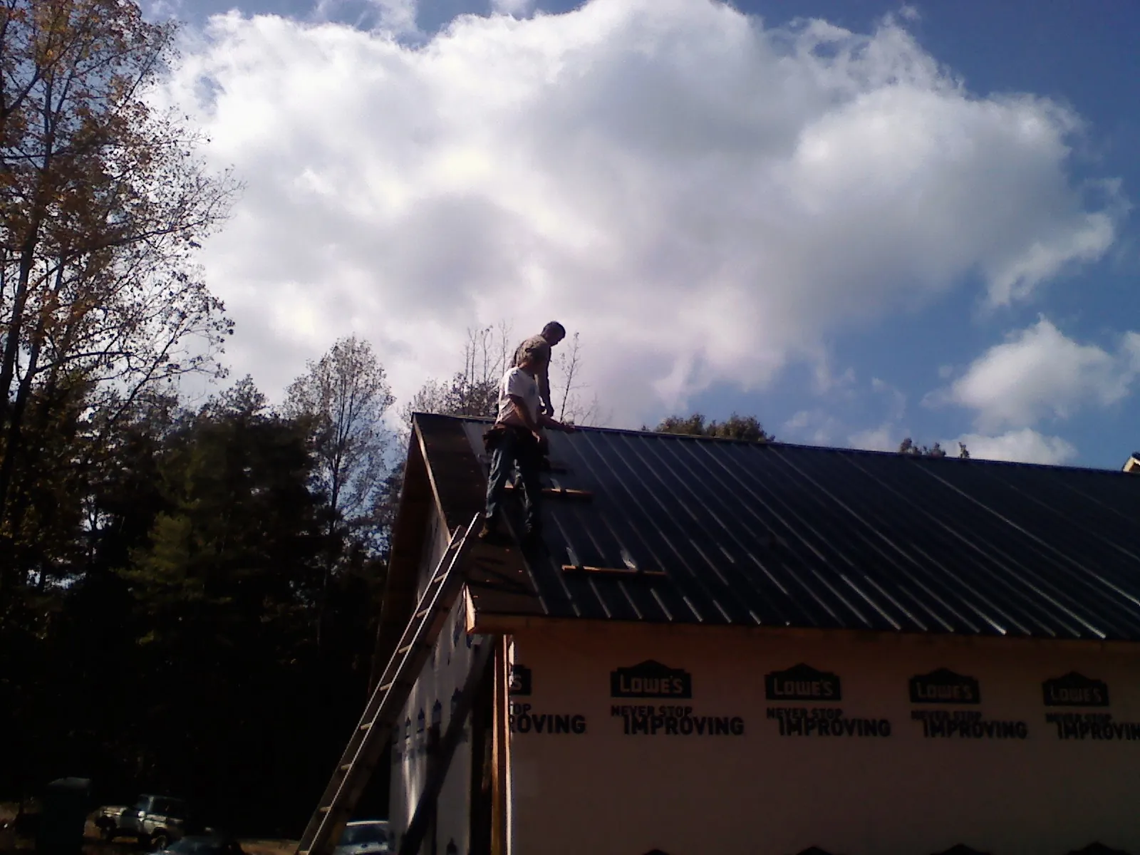Roofer fastening dark metal panels high against a cloudy sky, from a Roof Inspection job in Kirklin