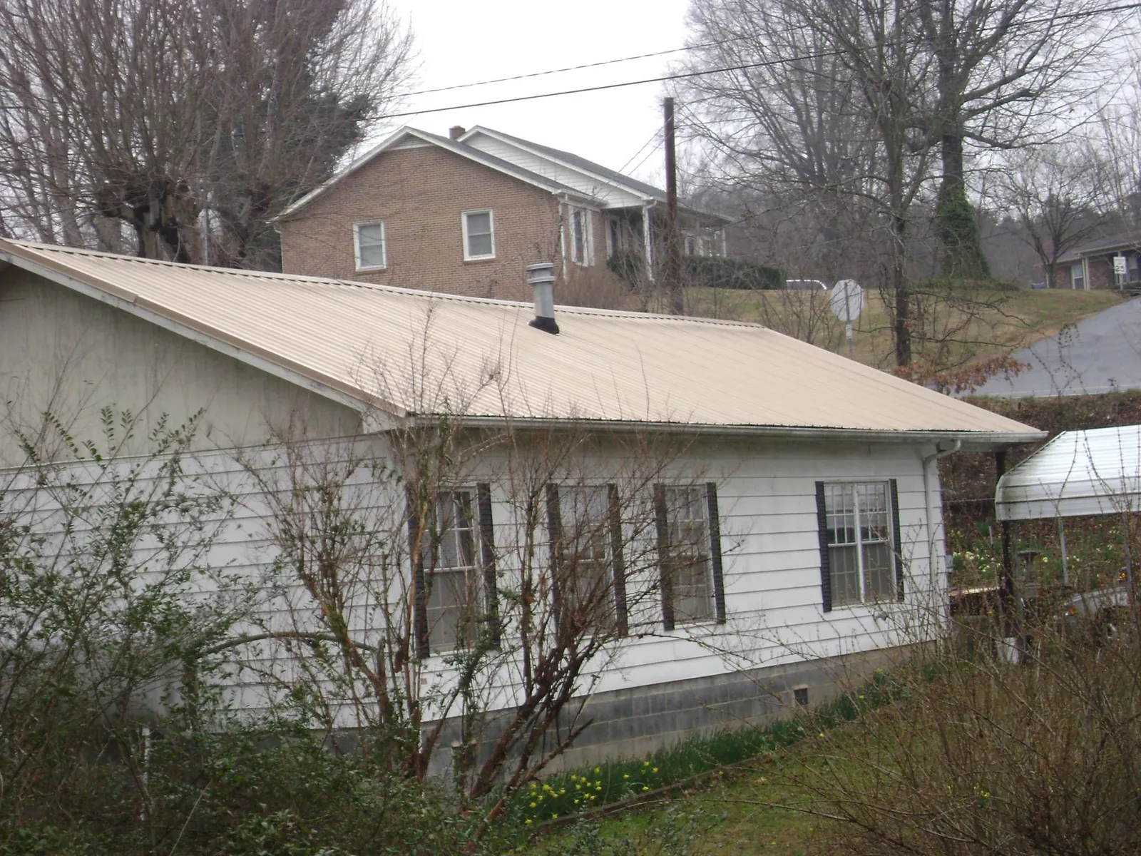 Tan metal roof on a white sided house set into a hillside — Commercial Roofing by Roofing Brothers in Kirklin