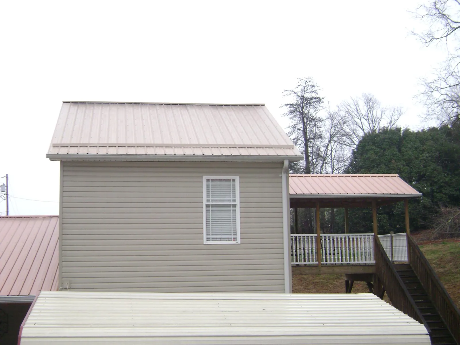 Tan metal roofs on a two story addition and attached porch, from a Roof Replacement job in Kirklin